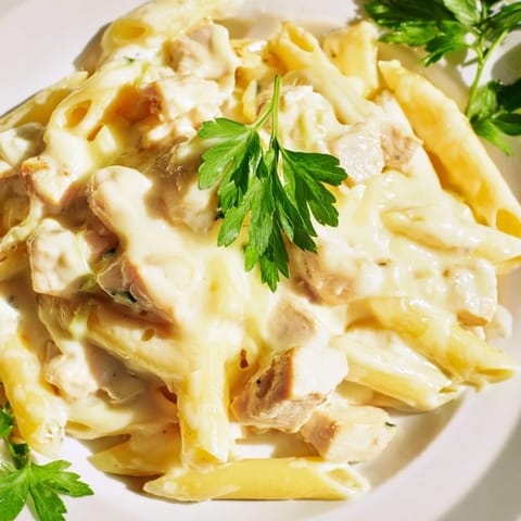 A close-up of a hearty Chicken Alfredo Casserole portion served on a white plate, garnished with fresh parsley. 