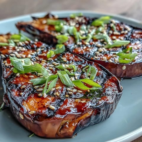 Golden-brown Miso Glazed Eggplant halves on a white plate, garnished with toasted sesame seeds and sliced green onions.  