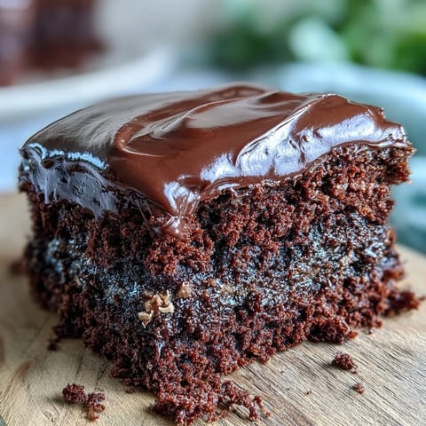 A slice of Easy Chocolate Fudge Cake shows a squidgy crumb on a plate with fresh raspberries nearby.