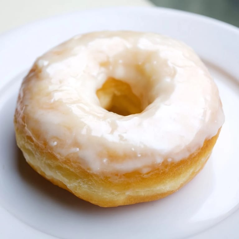 Fluffy American donuts, fresh from the fryer, glistening with sweet, vanilla glaze.