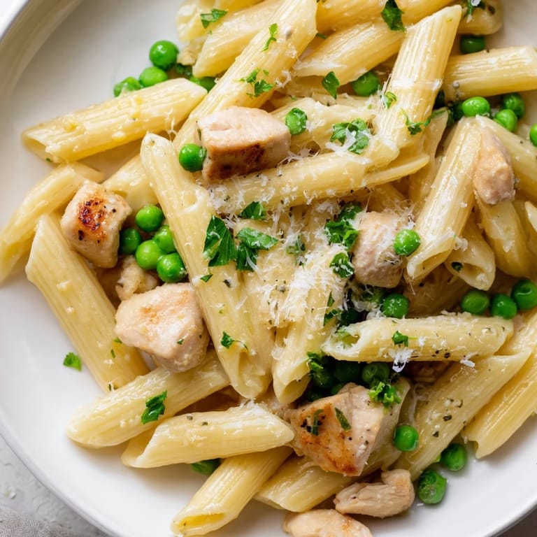 A close-up of steaming Pea & Mint Chicken Pasta, garnished with extra Parmesan cheese and chopped herbs on a rustic plate.