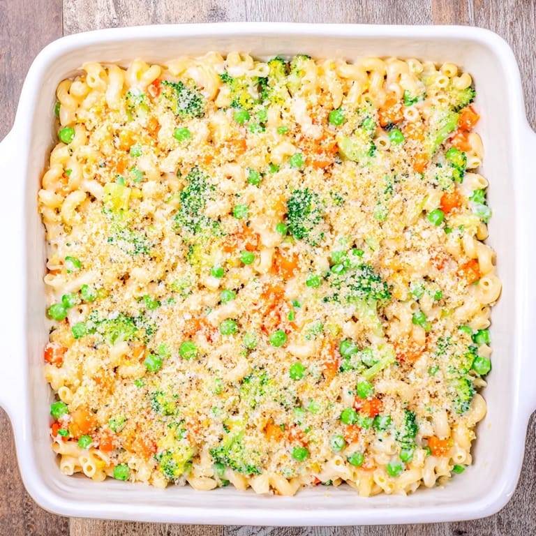 Close-up of Garden Veg Mac and Cheese, showing tender broccoli florets, diced carrots, and peas mixed with cheesy pasta under a crispy crumb topping.
