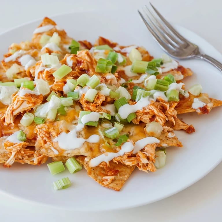 Buffalo Chicken Nachos loaded with shredded chicken, Monterey Jack cheese, and ranch dressing, garnished with tomatoes and cilantro for a flavorful appetizer.