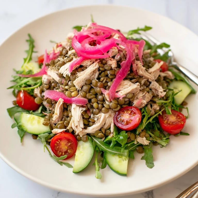 A close-up of Lentil & Chicken Spring Salad showing pickled onions, cherry tomatoes, and fresh greens on a plate.  