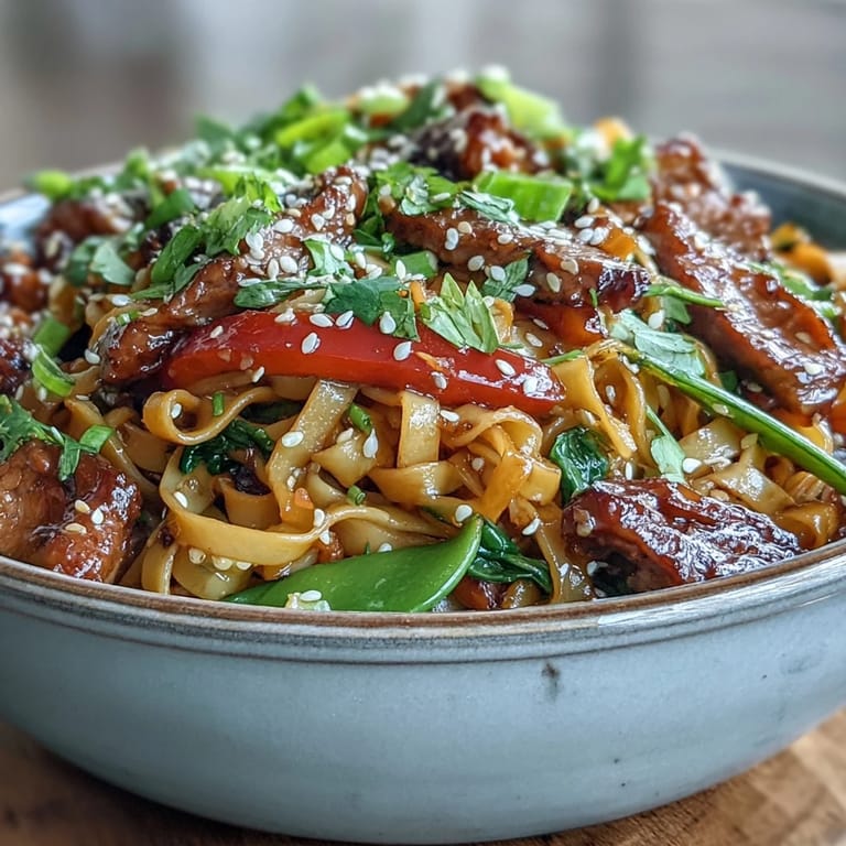 Close-up of Pork Noodle Stir-Fry with glossy noodles and vegetables, topped with fresh cilantro.